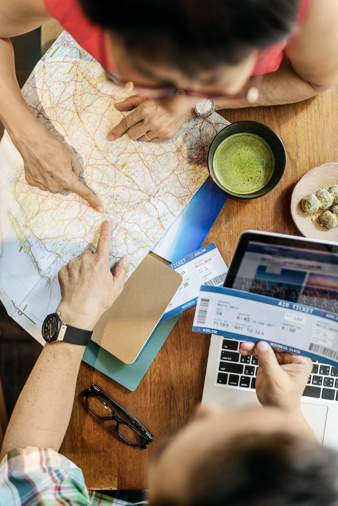 Travellers comparing a paper map beside travel documents and a laptop
